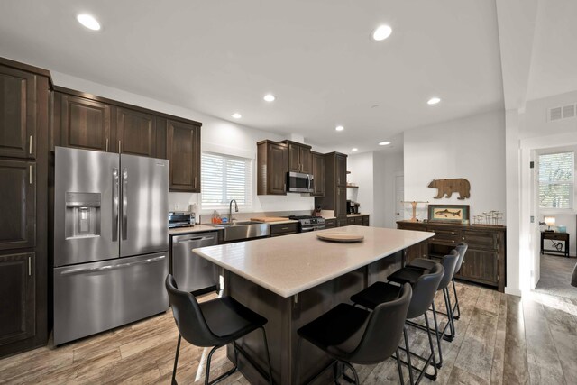 kitchen featuring dark brown cabinets, a kitchen bar, a kitchen island, light hardwood / wood-style floors, and appliances with stainless steel finishes