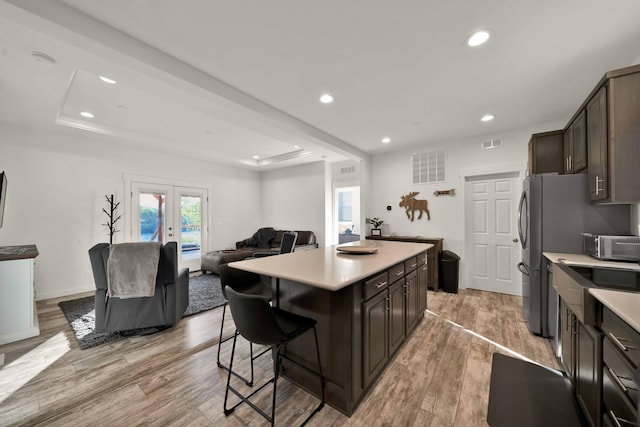 kitchen featuring a tray ceiling, french doors, a kitchen island, dark brown cabinetry, and light hardwood / wood-style floors