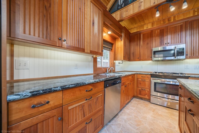 kitchen featuring stainless steel appliances, a sink, brown cabinets, decorative backsplash, and dark stone counters