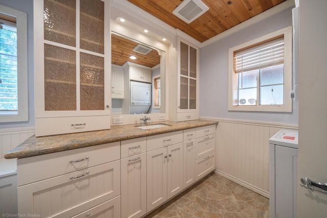 bathroom featuring a wainscoted wall, a wealth of natural light, stacked washer / drying machine, visible vents, and wood ceiling