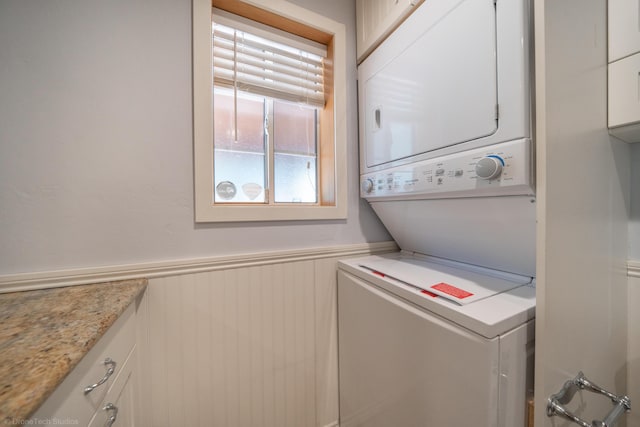 laundry room featuring wainscoting, cabinet space, and stacked washing maching and dryer