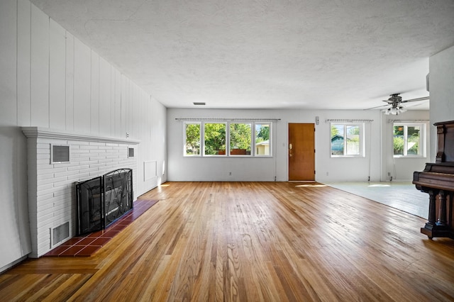 unfurnished living room with a brick fireplace, a healthy amount of sunlight, visible vents, and hardwood / wood-style floors