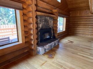 unfurnished living room featuring log walls, wood-type flooring, vaulted ceiling, and a wood stove