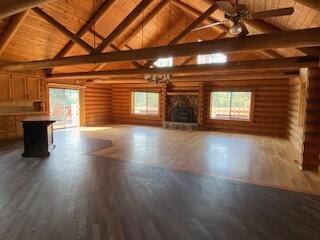 unfurnished living room featuring beam ceiling, wood-type flooring, plenty of natural light, and rustic walls