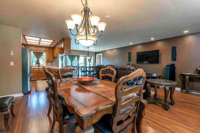 dining space with a skylight, light wood-type flooring, and an inviting chandelier