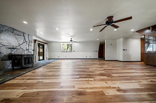 unfurnished living room featuring a wood stove, ceiling fan, and light wood-type flooring