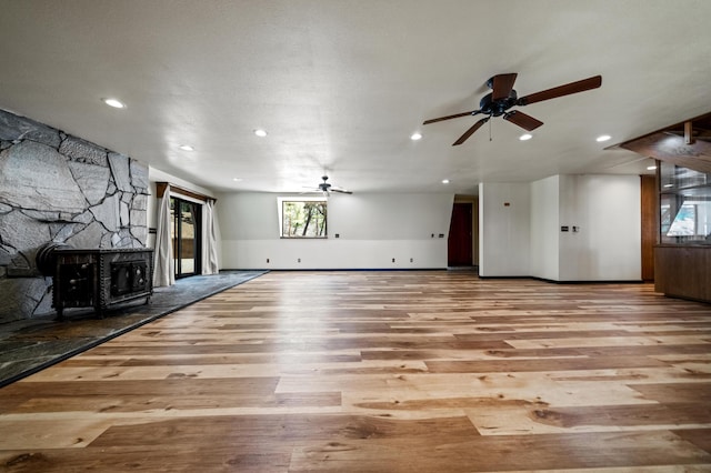 unfurnished living room with baseboards, a ceiling fan, wood finished floors, a stone fireplace, and recessed lighting