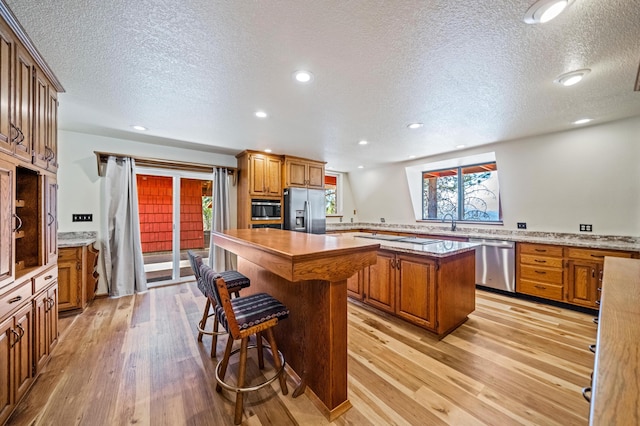 kitchen featuring appliances with stainless steel finishes, brown cabinetry, light wood-type flooring, and a kitchen island