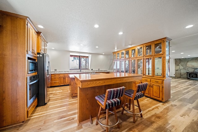 kitchen with stainless steel appliances, a fireplace, a kitchen island, light wood-type flooring, and a textured ceiling