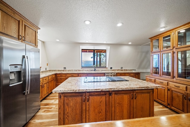 kitchen with brown cabinets, a kitchen island, a sink, and stainless steel fridge with ice dispenser