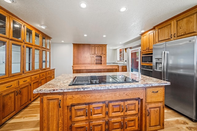 kitchen with light wood-style flooring, stainless steel appliances, a kitchen island, brown cabinets, and glass insert cabinets