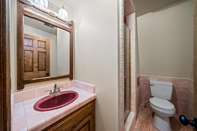 bathroom featuring a shower with shower door, tile walls, tile patterned flooring, toilet, and vanity