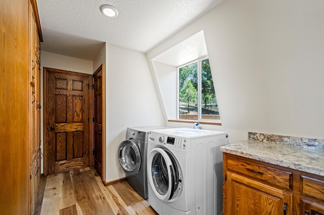 clothes washing area with a textured ceiling, independent washer and dryer, and light hardwood / wood-style floors