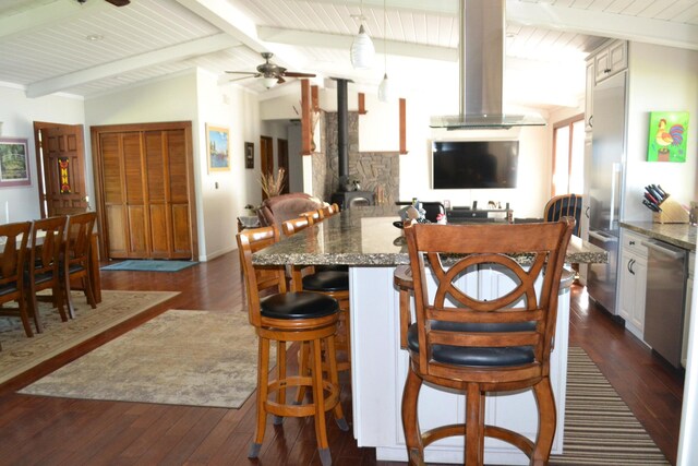 kitchen featuring stone counters, ceiling fan, dark wood-type flooring, wall chimney exhaust hood, and vaulted ceiling with beams