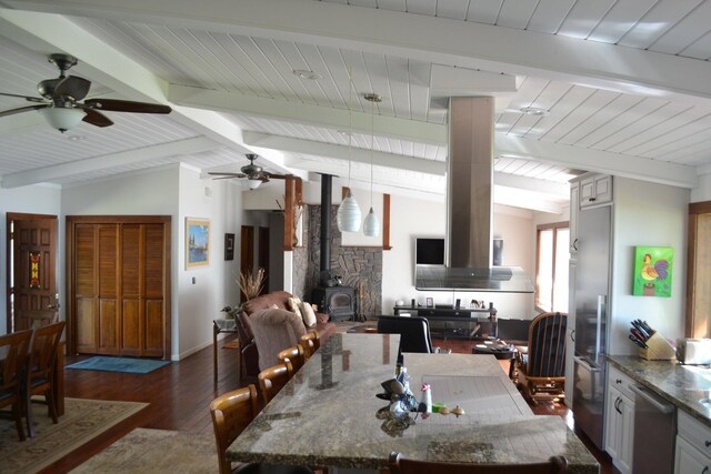 dining area featuring a wood stove, lofted ceiling with beams, dark wood-type flooring, and ceiling fan