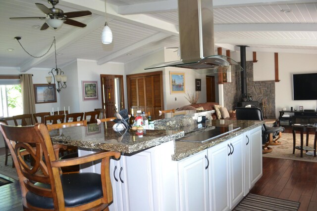 kitchen with dark wood-type flooring, white cabinets, a wood stove, extractor fan, and vaulted ceiling with beams