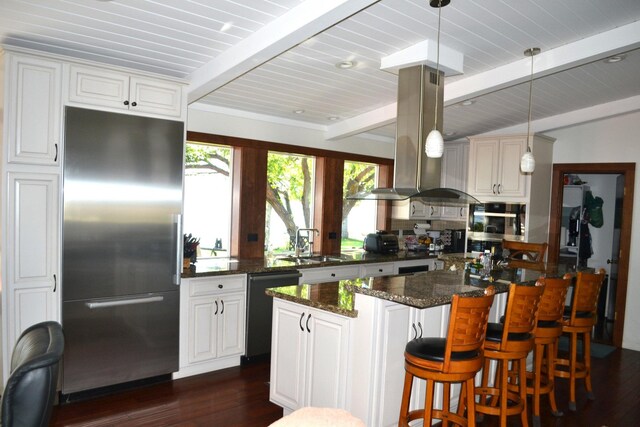 kitchen featuring island exhaust hood, stainless steel appliances, dark stone countertops, beamed ceiling, and dark wood-type flooring