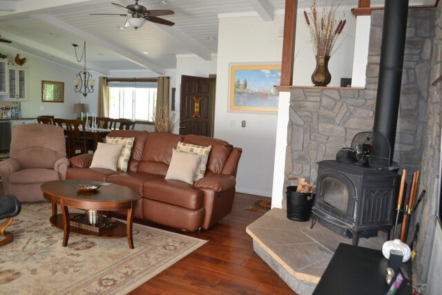 living room with ceiling fan, dark wood-type flooring, vaulted ceiling with beams, and a wood stove