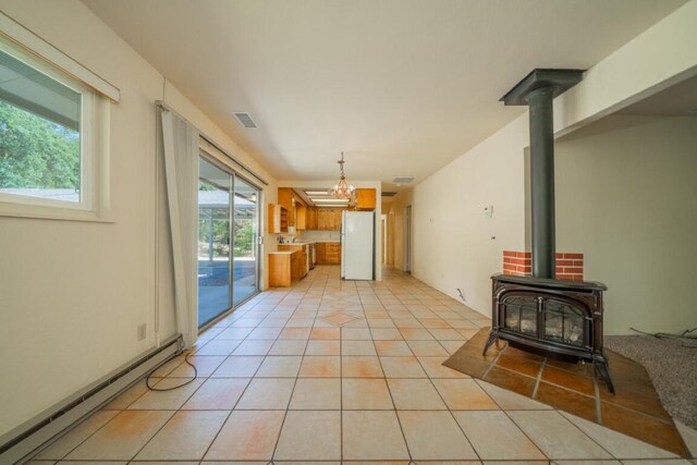 unfurnished living room with a chandelier, a wood stove, a baseboard heating unit, and light tile patterned flooring