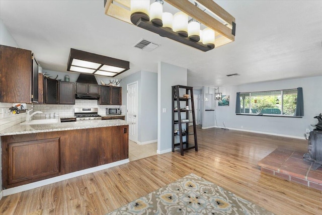 kitchen featuring light wood-type flooring, appliances with stainless steel finishes, light stone counters, sink, and kitchen peninsula