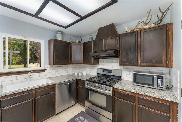 kitchen with light tile patterned floors, light stone countertops, stainless steel appliances, sink, and tasteful backsplash