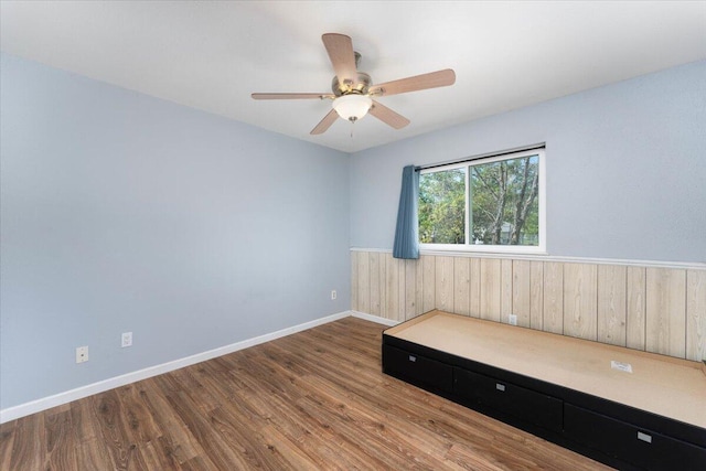 unfurnished room featuring wood walls, wood-type flooring, and ceiling fan