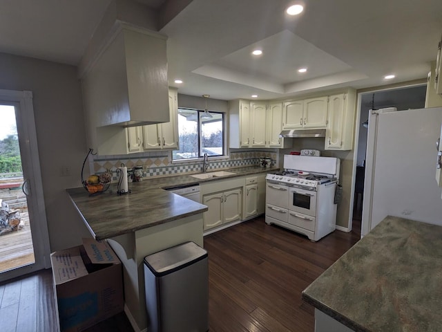 kitchen featuring white appliances, kitchen peninsula, dark wood-type flooring, a raised ceiling, and sink