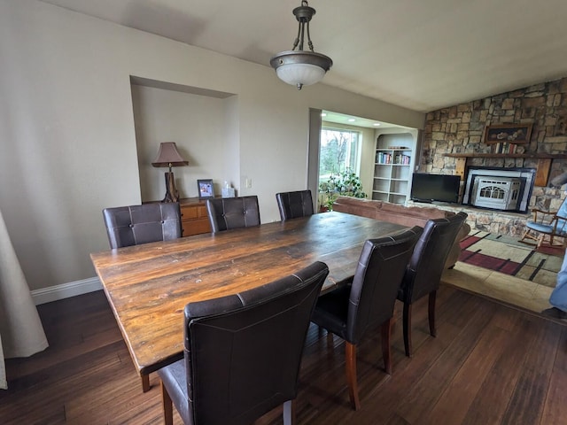 dining space with dark wood-type flooring and a stone fireplace