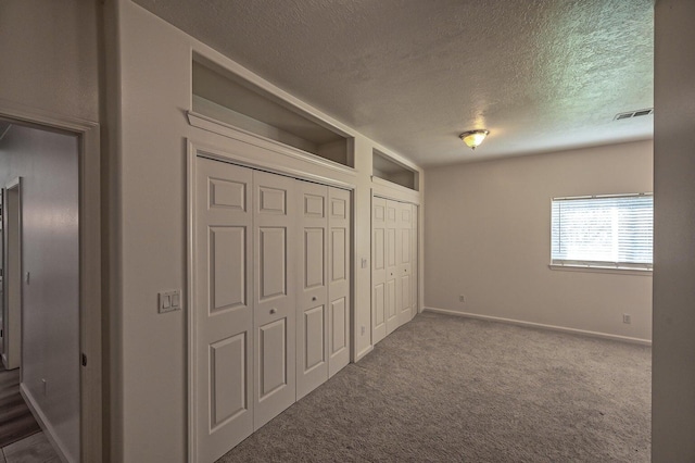 unfurnished bedroom featuring a textured ceiling, carpet floors, and two closets