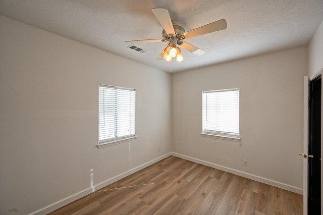 unfurnished room with a textured ceiling, light wood-type flooring, ceiling fan, and a healthy amount of sunlight