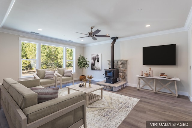 living room with ceiling fan, wood-type flooring, ornamental molding, and a wood stove