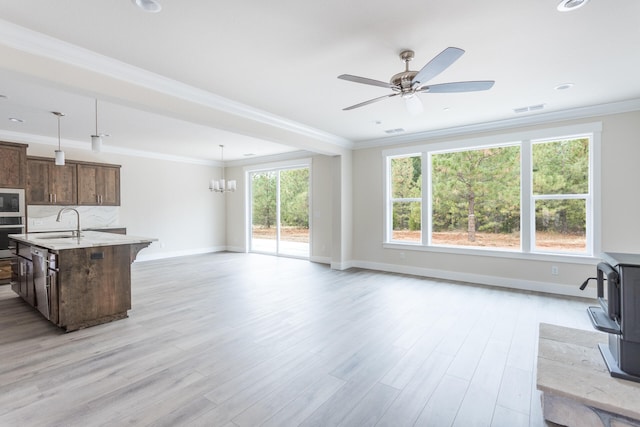 kitchen with light hardwood / wood-style floors, appliances with stainless steel finishes, decorative light fixtures, and a center island with sink