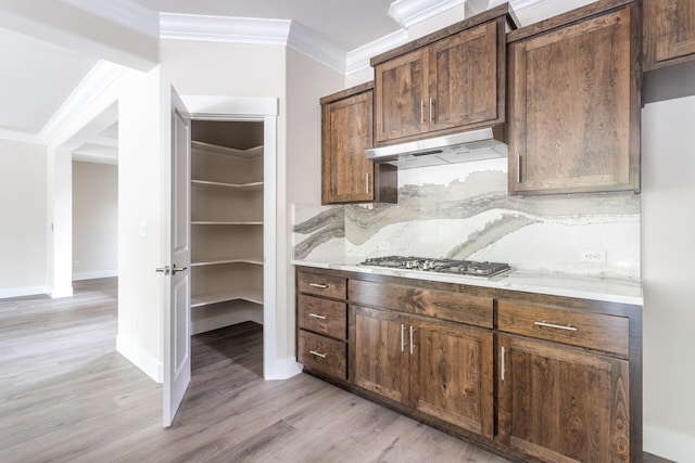 kitchen with ornamental molding, dark brown cabinetry, light wood-type flooring, stainless steel gas stovetop, and tasteful backsplash