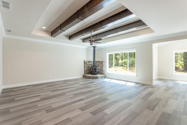 unfurnished living room with ceiling fan, beam ceiling, a healthy amount of sunlight, and a wood stove