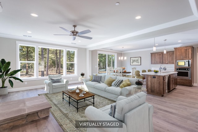 living room with light hardwood / wood-style flooring, ornamental molding, sink, and ceiling fan with notable chandelier