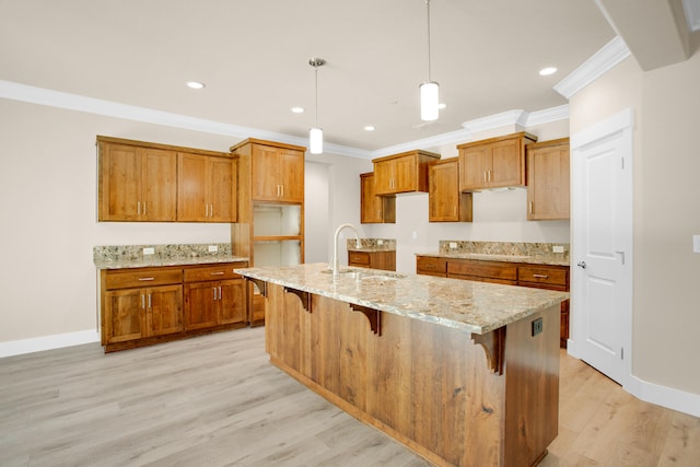 kitchen featuring sink, decorative light fixtures, a breakfast bar area, a center island with sink, and light wood-type flooring