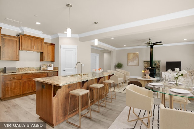 kitchen with a center island with sink, light hardwood / wood-style floors, sink, and hanging light fixtures