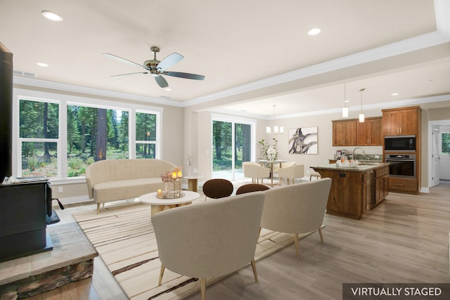 living room with ceiling fan with notable chandelier, light hardwood / wood-style flooring, crown molding, and sink