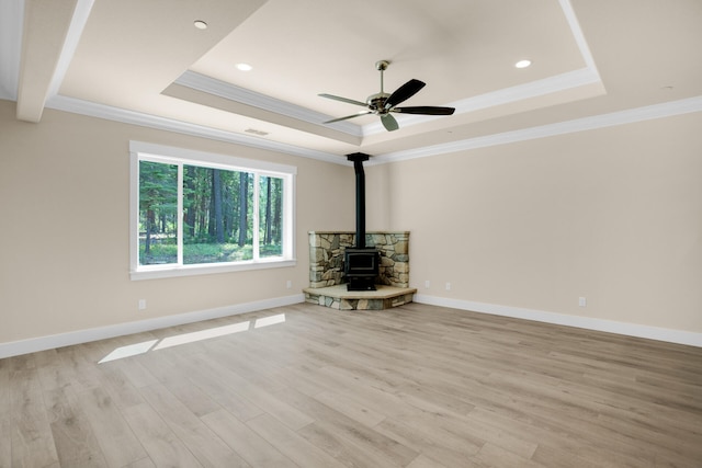 unfurnished living room featuring a wood stove, ornamental molding, a raised ceiling, light hardwood / wood-style floors, and ceiling fan