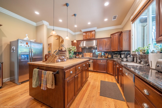 kitchen with sink, butcher block counters, wall chimney exhaust hood, light hardwood / wood-style floors, and stainless steel appliances