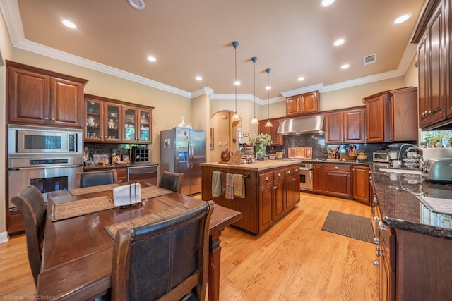 kitchen featuring appliances with stainless steel finishes, backsplash, crown molding, light wood-type flooring, and wall chimney range hood