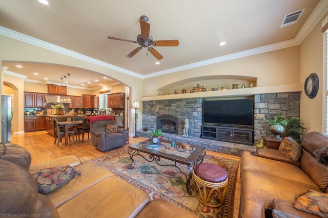 living room with ceiling fan, light hardwood / wood-style flooring, ornamental molding, and a fireplace