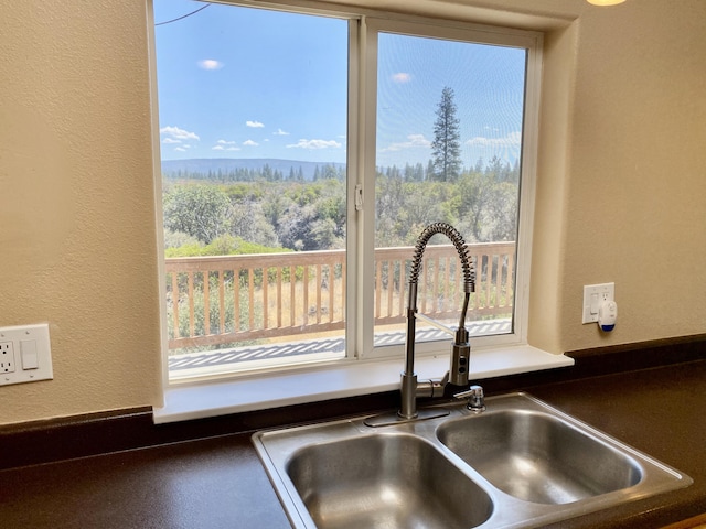 interior details featuring dark countertops, a view of trees, a textured wall, and a sink