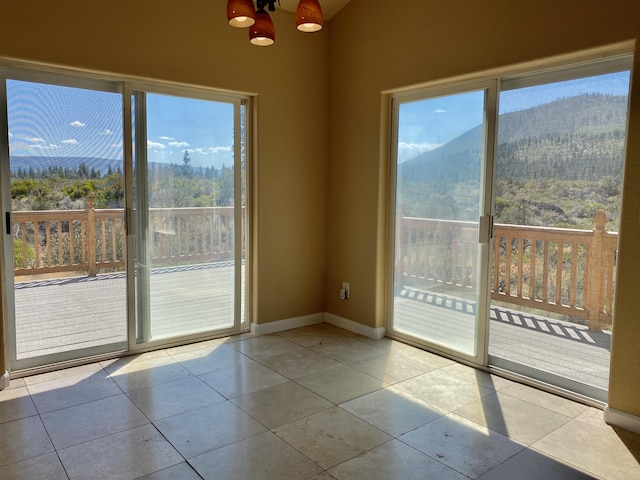 spare room featuring tile patterned floors, a view of trees, baseboards, and a chandelier