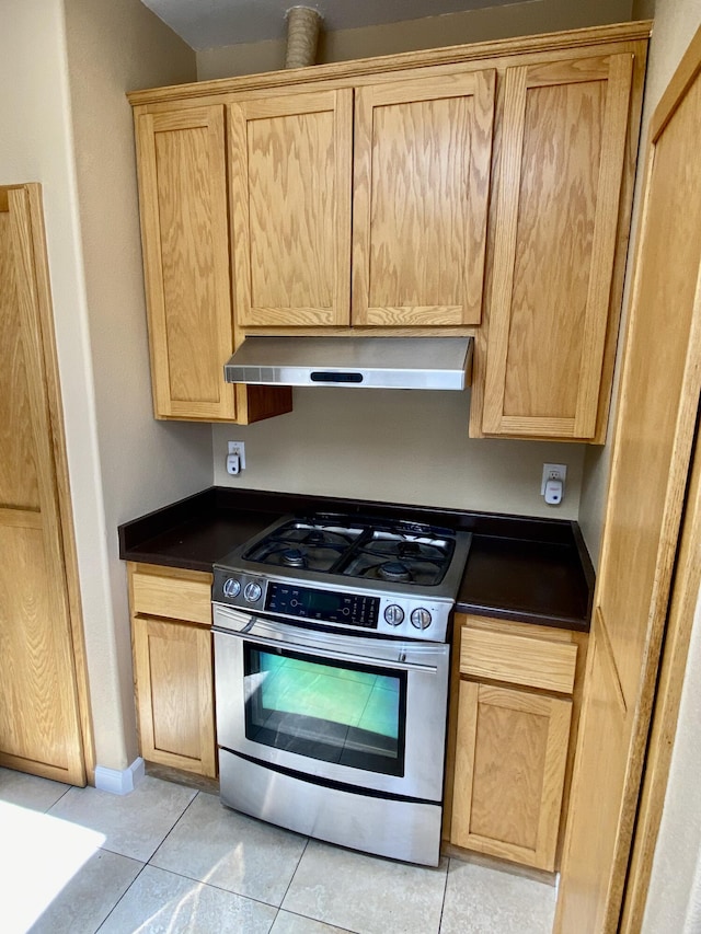 kitchen with dark countertops, light tile patterned floors, exhaust hood, and stainless steel gas range