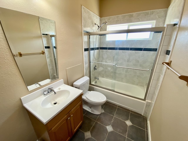 full bathroom with vanity, tile patterned floors, toilet, a textured wall, and combined bath / shower with glass door