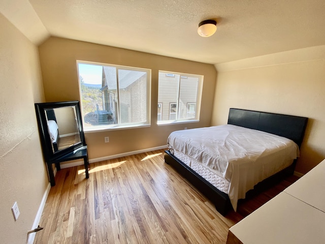 bedroom featuring baseboards, a textured ceiling, lofted ceiling, and wood finished floors