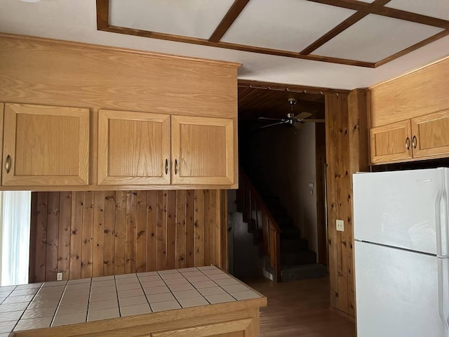 kitchen with hardwood / wood-style floors, tile countertops, wood walls, ceiling fan, and white refrigerator