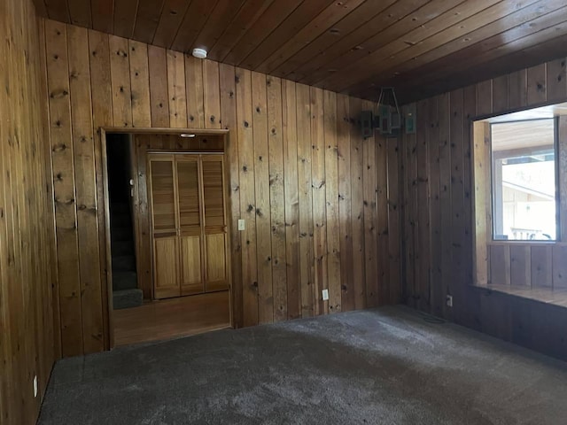 carpeted empty room featuring wood ceiling and wood walls