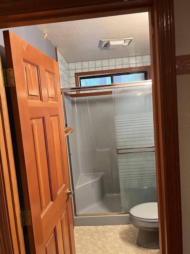 bathroom with toilet, a shower with door, and a textured ceiling